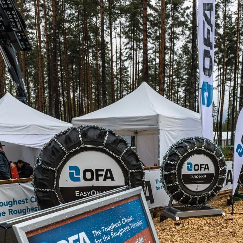 White canopy tents set up at an outdoor trade event with OFA tire chain displays, promotional banners, and a forest backdrop.