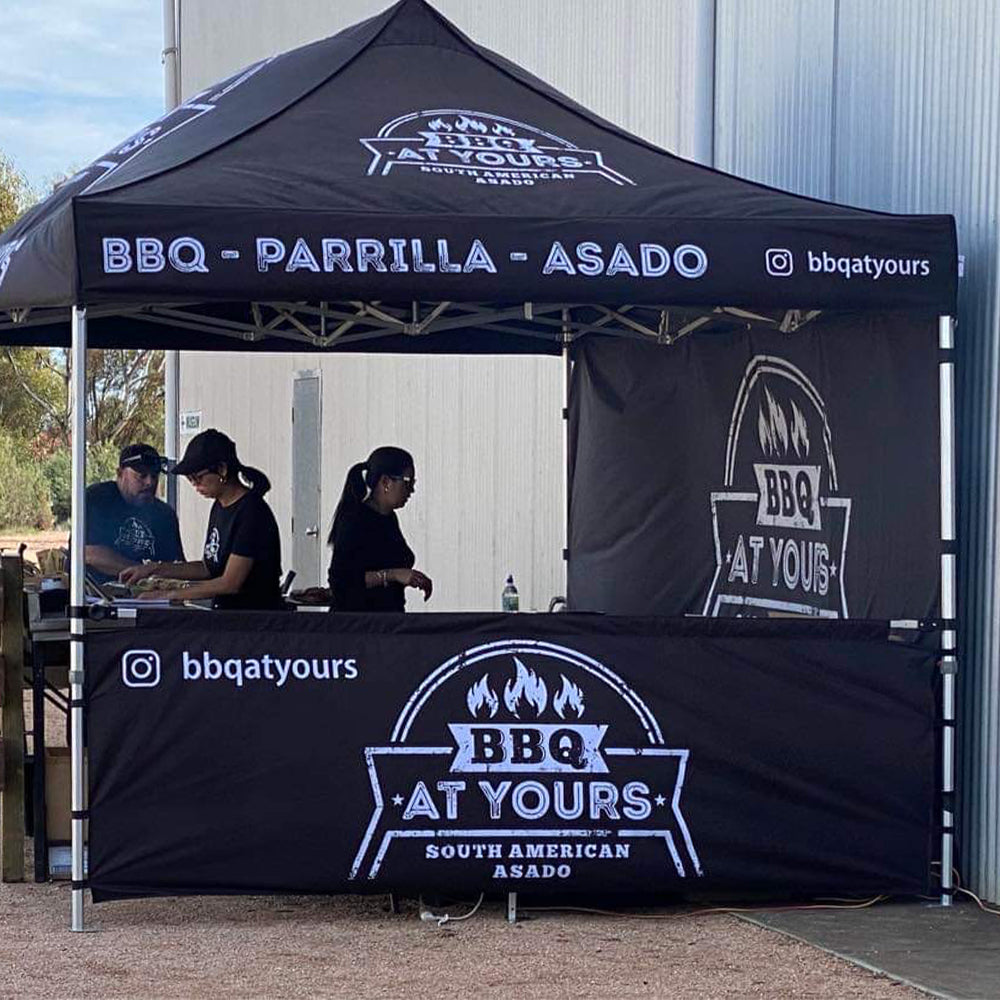 canopy tent set up with custom-printed half wall featuring "BBQ At Yours" branding.