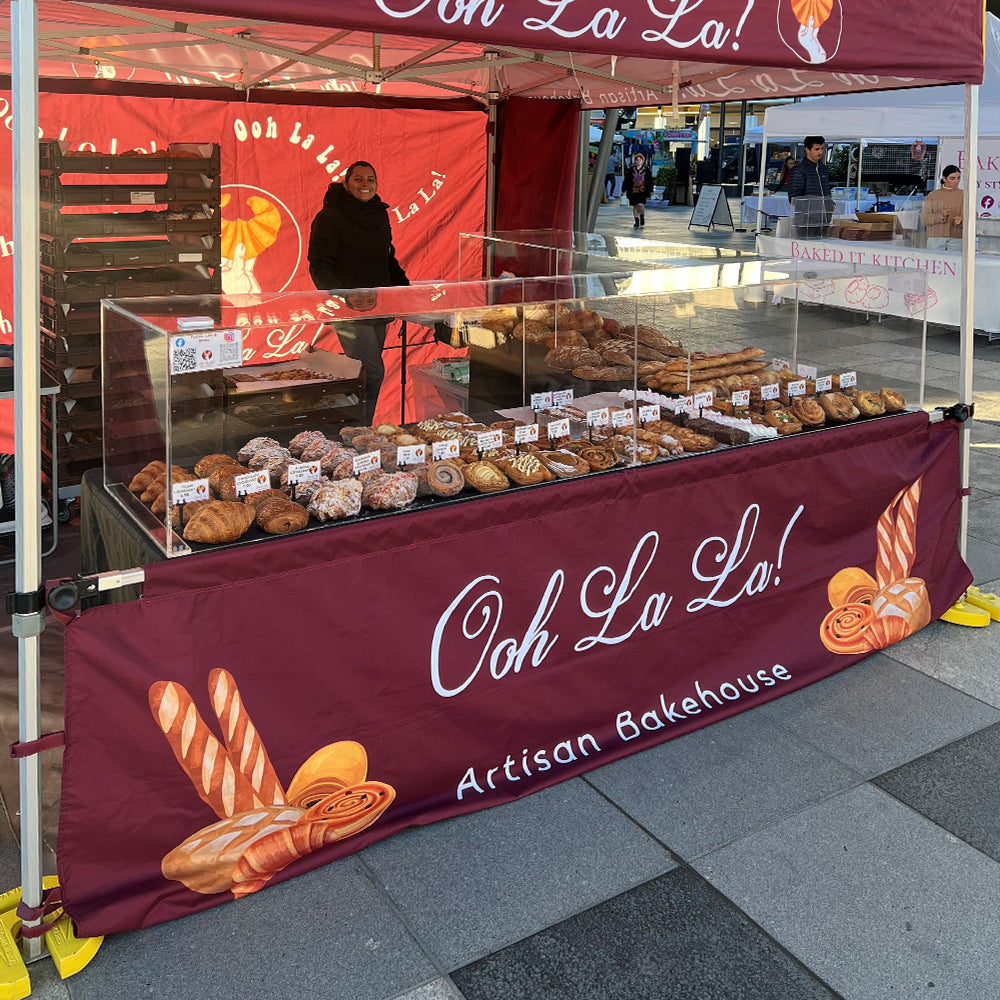 canopy tent set up with custom-printed half wall featuring "Ooh Laa Laa Artisan Bakehouse" branding.