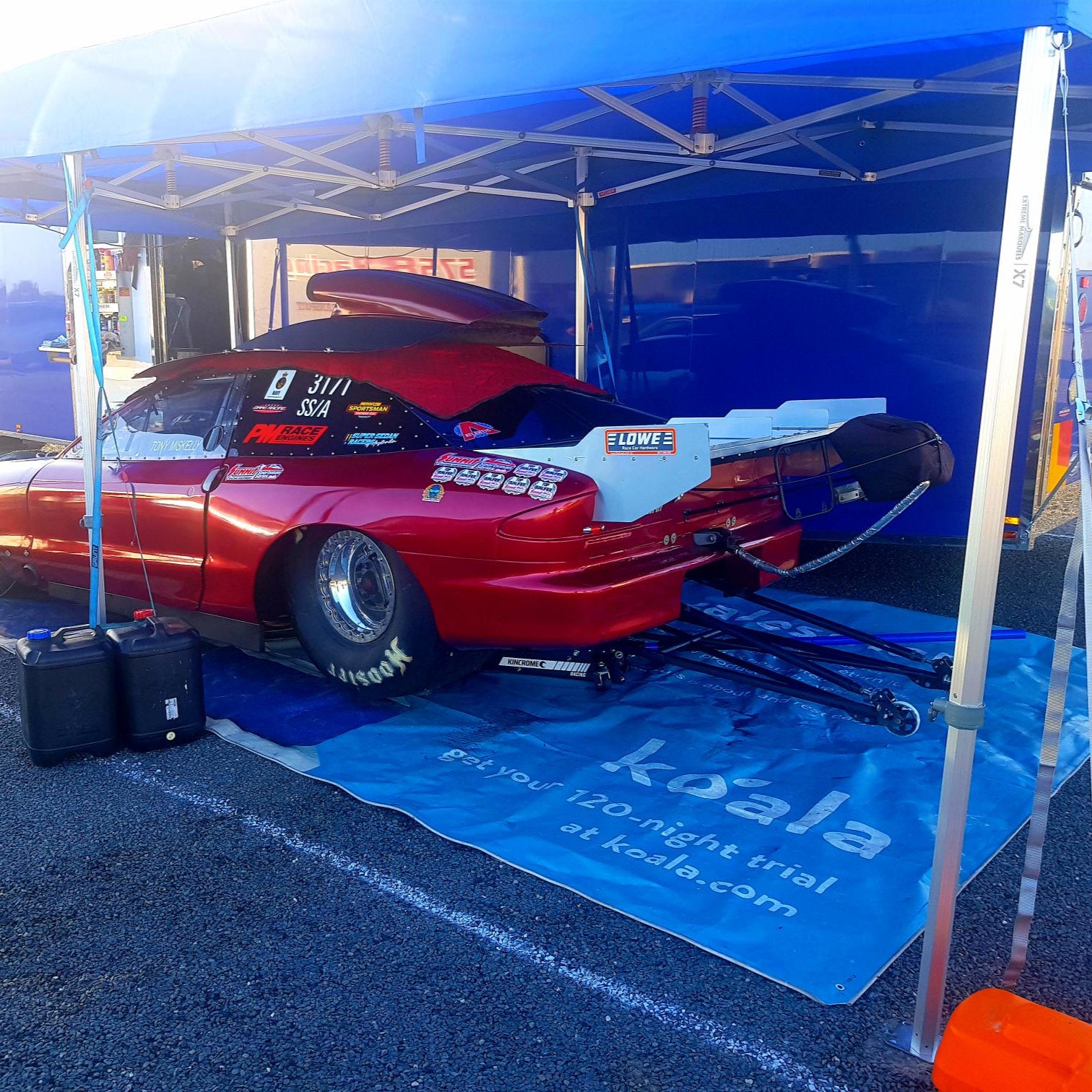 Blue pop-up canopy tent providing shade for a red drag racing car at a motorsport event