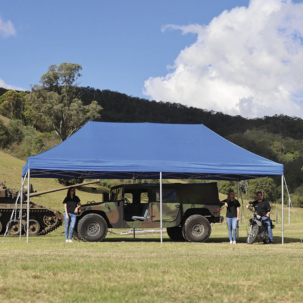 Large blue 13x26 ft pop-up canopy sheltering setup in an open field with hills and trees in the background.